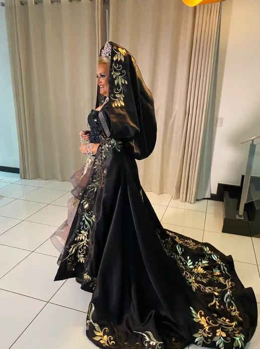 Vestido preto com bordados dourados e cauda, visto de perfil